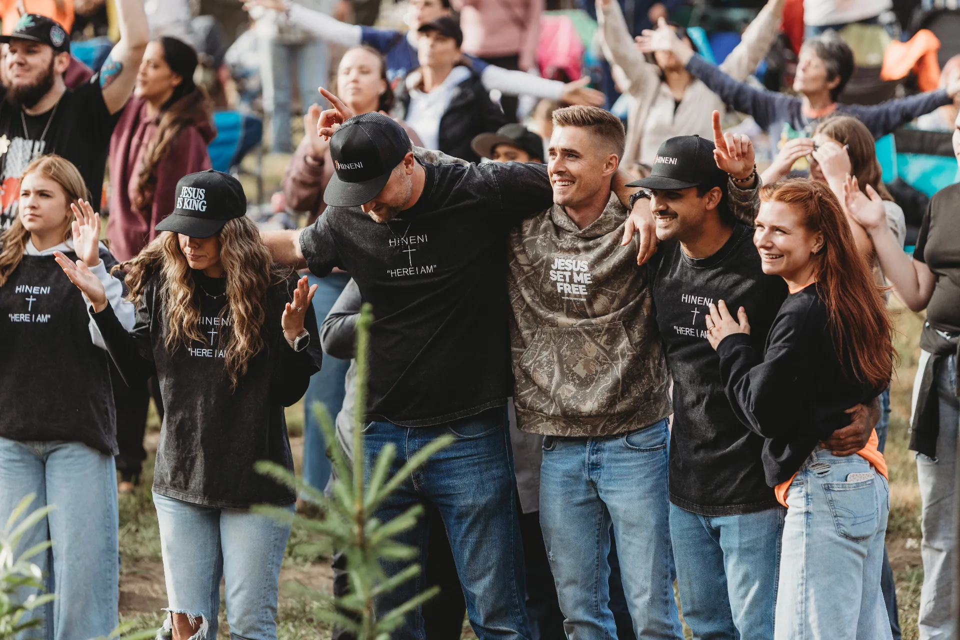 A gathering of people worshipping with hands raised in an open field