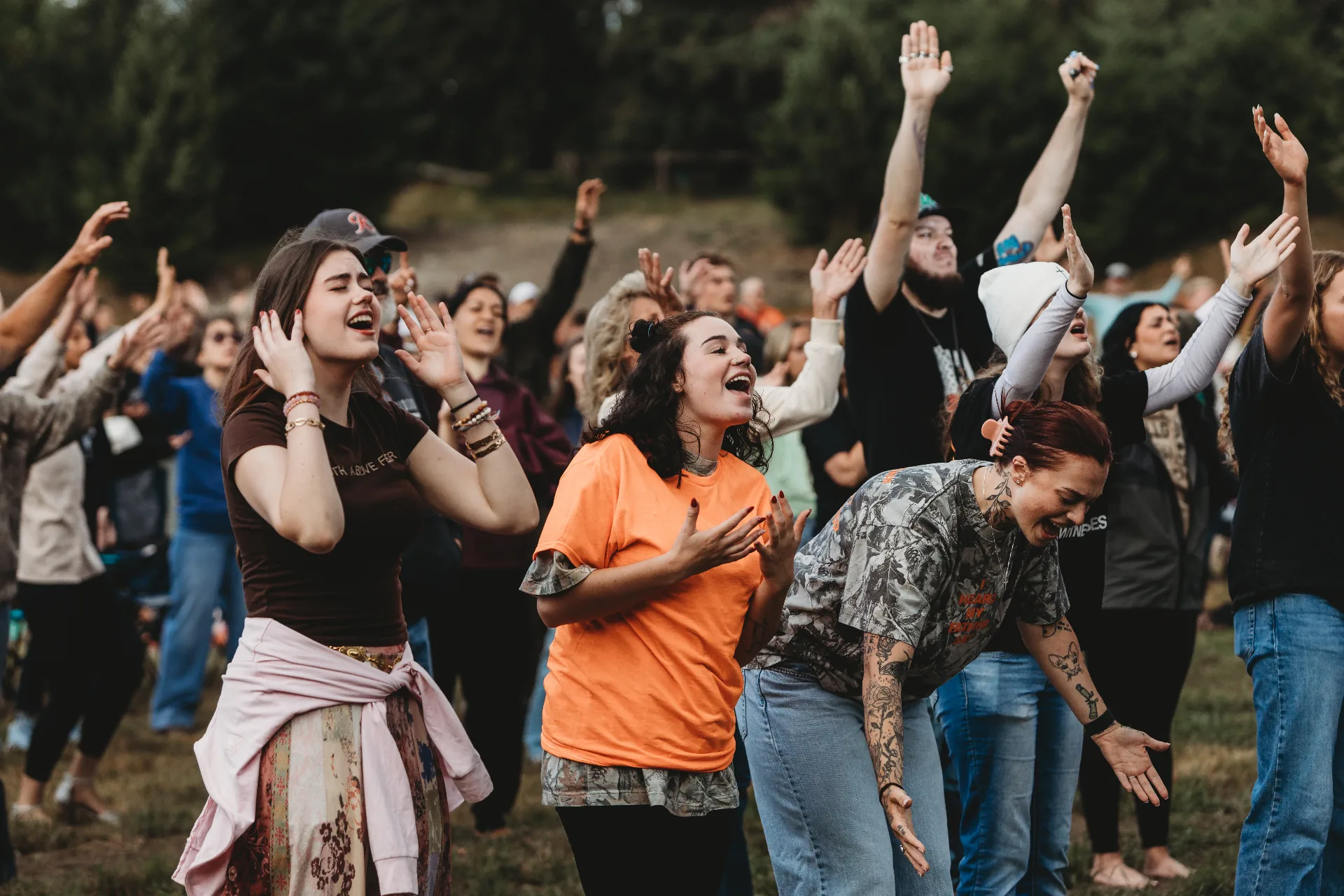 A crowd worshipping outdoors with hands raised at Revival at the Farm